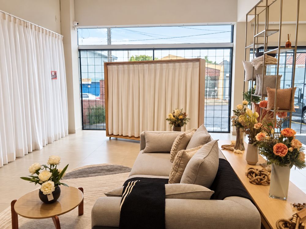 Interior do showroom Casa Nova Requinte com cortinas de voil, sofá e arranjos florais